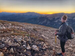 Eine Wanderin, die auf einem Berg steht and den Sonnenaufgang betrachtet